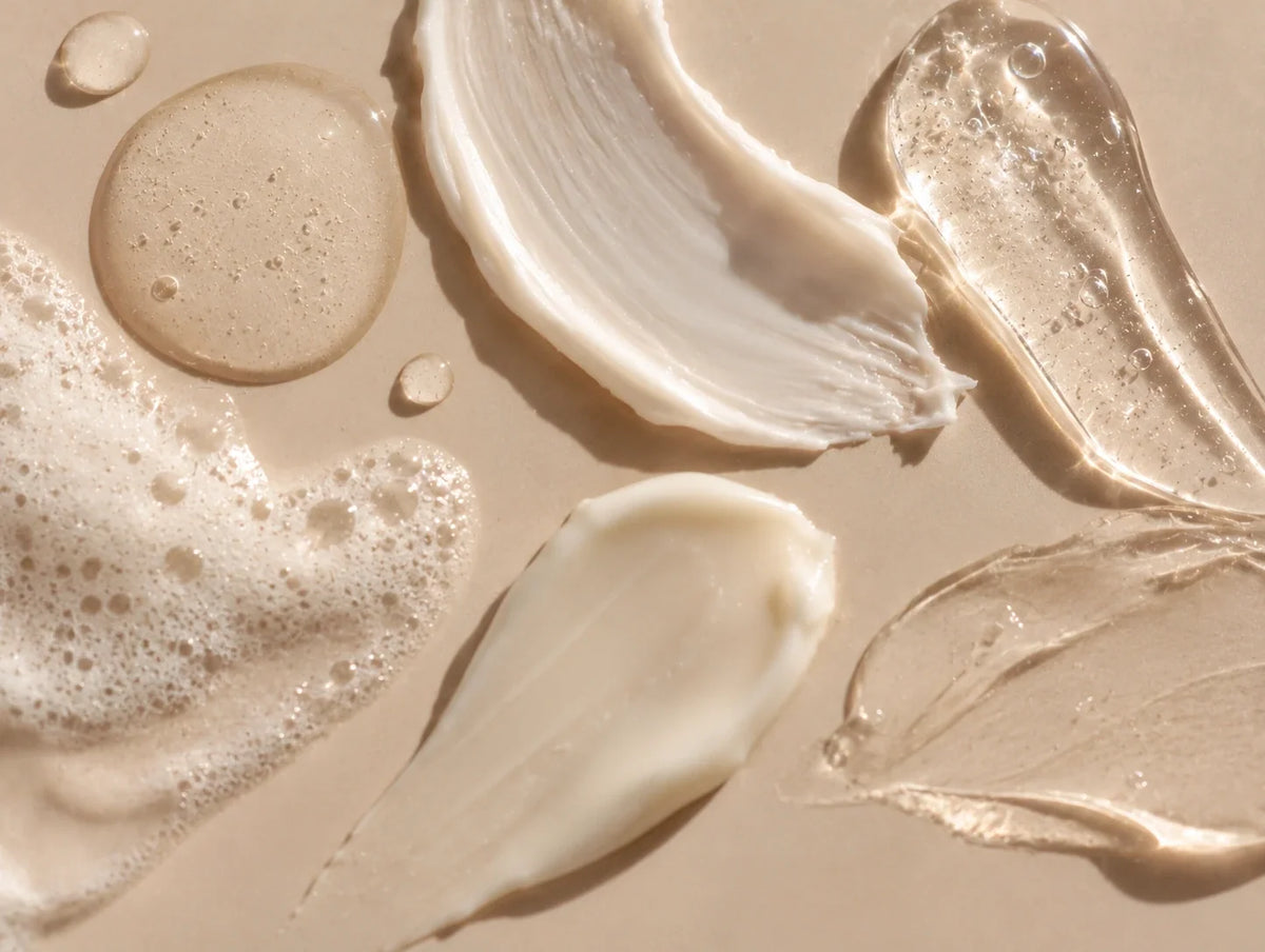Gros plan sur différentes textures de soins visage : crème hydratante, sérum transparent, gel et mousse nettoyante, sur un fond beige lumineux.
