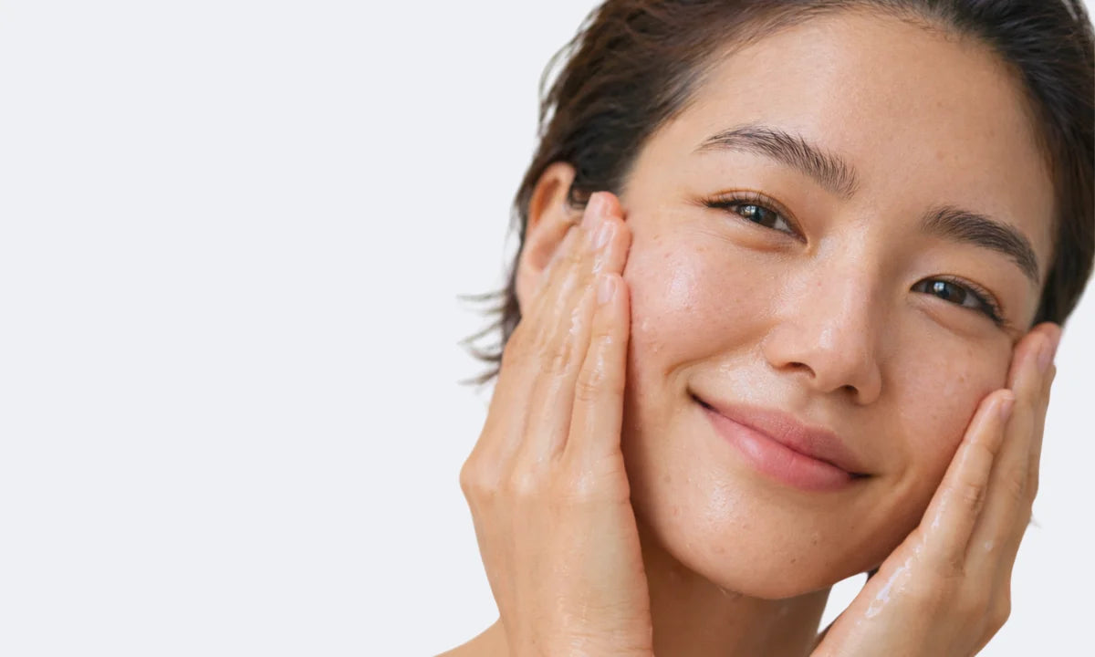 Femme souriante appliquant un soin visage sur une peau légèrement brillante, illustrant une routine pour les peaux sujettes aux imperfections, excès de sébum et points noirs.