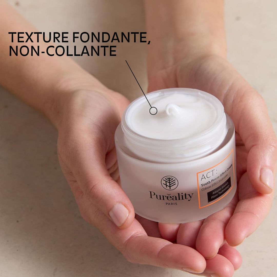 Image promotionnelle d’une crème visage tenue dans deux mains, avec le pot ouvert montrant une texture blanche onctueuse. Texte indiquant « Texture fondante, non-collante », avec un repère pointant la crème. Produit « Puréality – Crème Éclat Régénérante » visible sur le pot.